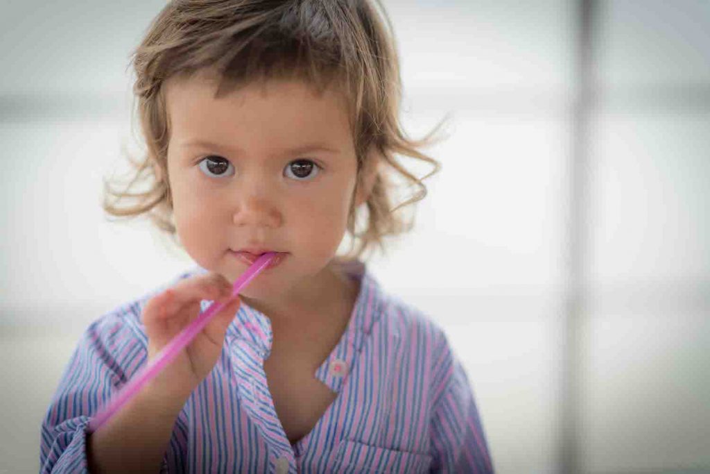 Close up of young toddler girl chewing on a straw
