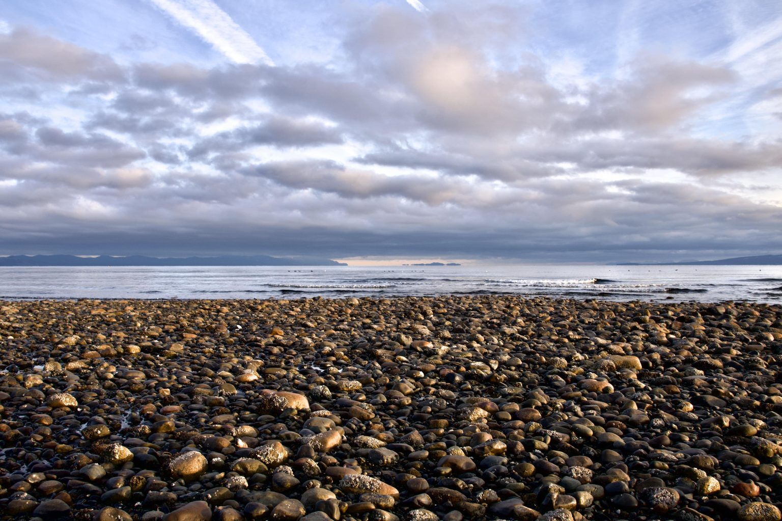 Rocky pebble shore at Point Holmes in Comox under a cloudy sky overlooking calm ocean waters